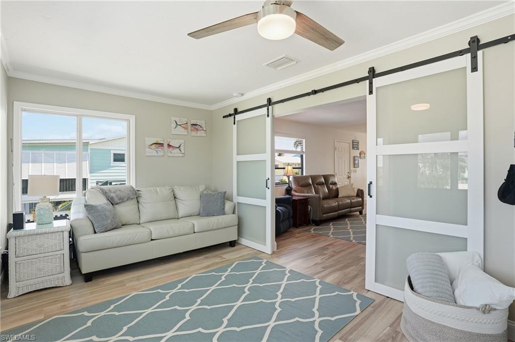 Den with a barn door, crown molding, ceiling fan, and light wood-style floors - Virtually Edited Image
