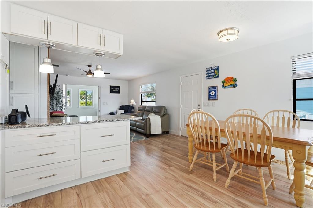 Kitchen featuring white cabinets, light stone counters, ceiling fan, and open floor plan - Virtually Edited Image