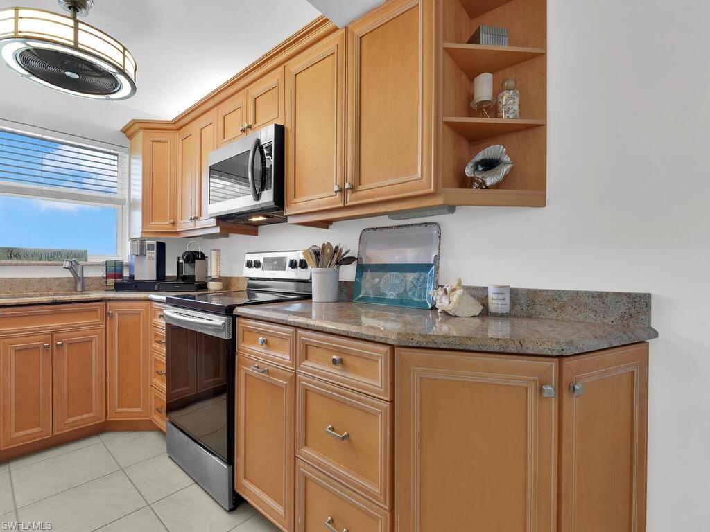 Kitchen featuring appliances with stainless steel finishes, open shelves, dark stone counters, and light tile patterned floors