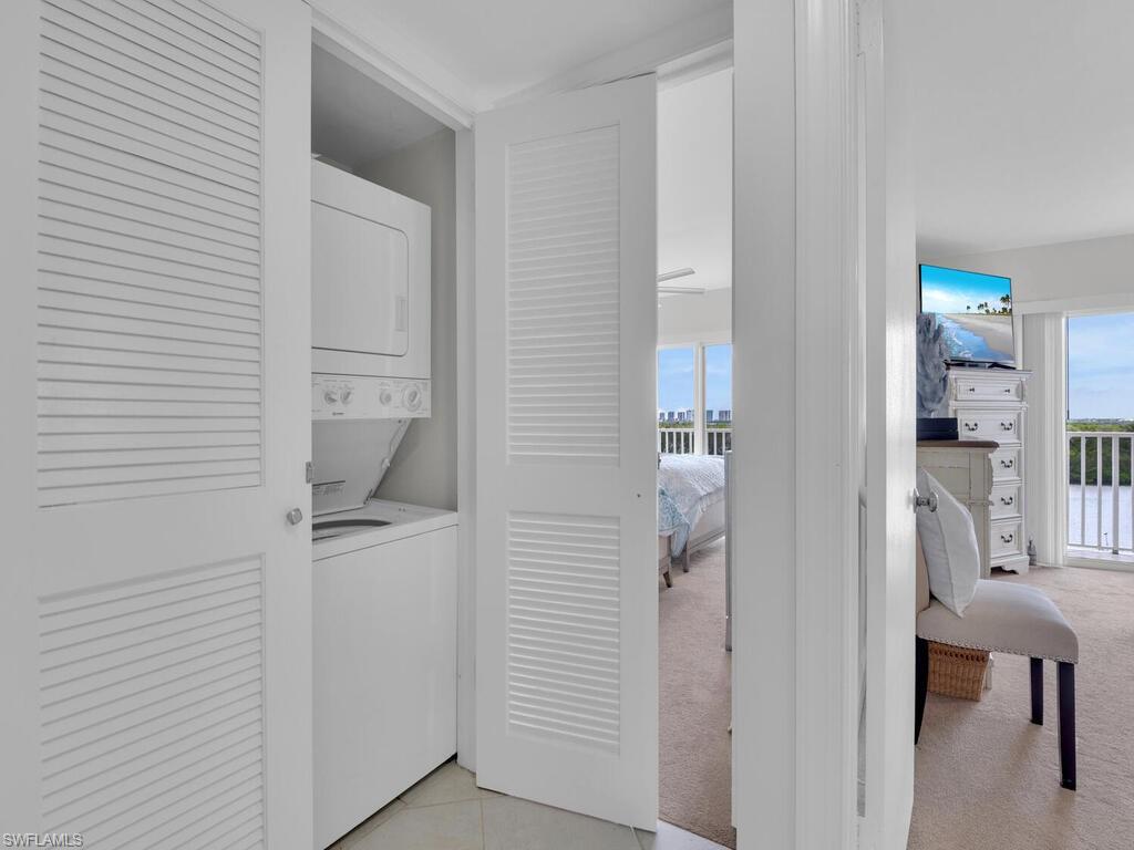 Laundry room with estacked washer and dryer, light carpet, and light tile patterned floors