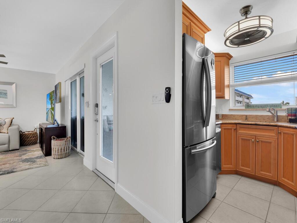 Kitchen featuring light tile patterned floors, freestanding refrigerator, light stone countertops, and brown cabinetry
