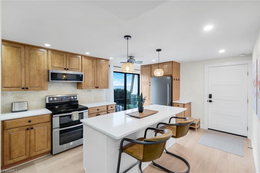 Kitchen featuring appliances with stainless steel finishes, a kitchen breakfast bar, brown cabinets, decorative light fixtures, and light wood-type flooring