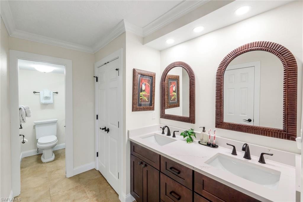 Full bathroom featuring double vanity, crown molding, light tile patterned flooring, and a closet