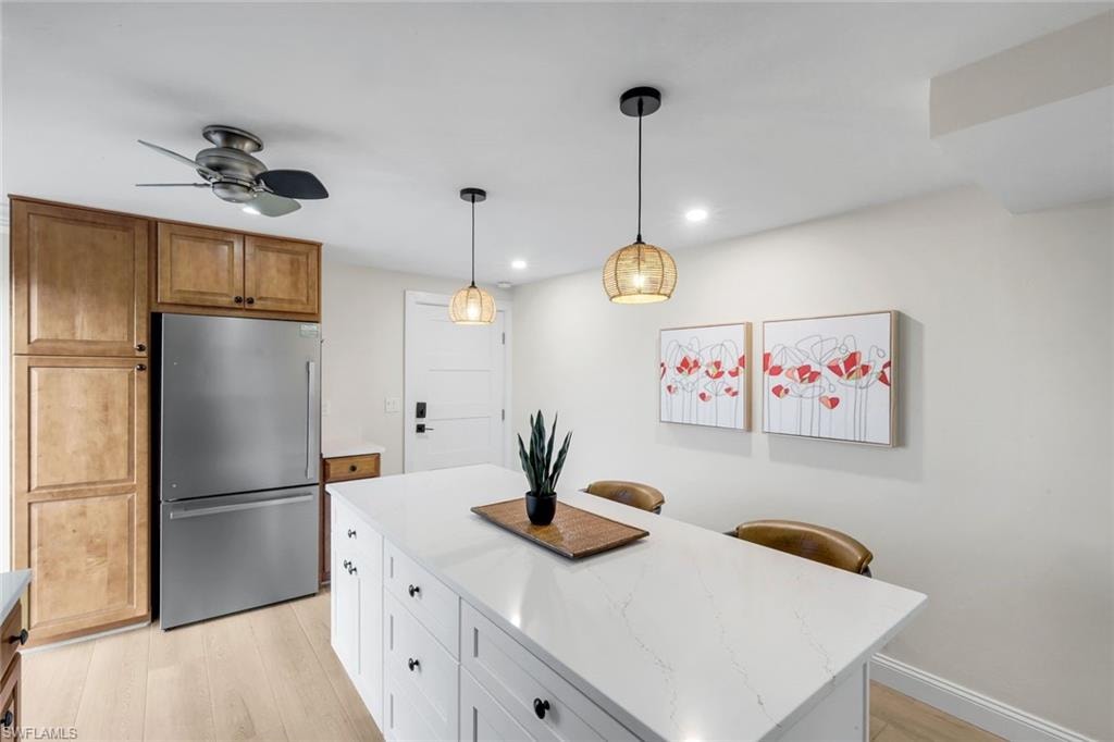 Kitchen featuring freestanding refrigerator, a center island, hanging light fixtures, light wood-style flooring, and light stone countertops