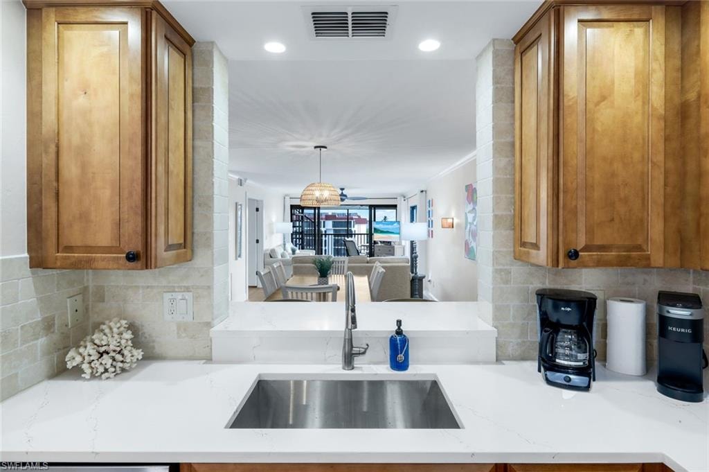 Kitchen with tasteful backsplash, light stone counters, brown cabinetry, recessed lighting, and hanging light fixtures