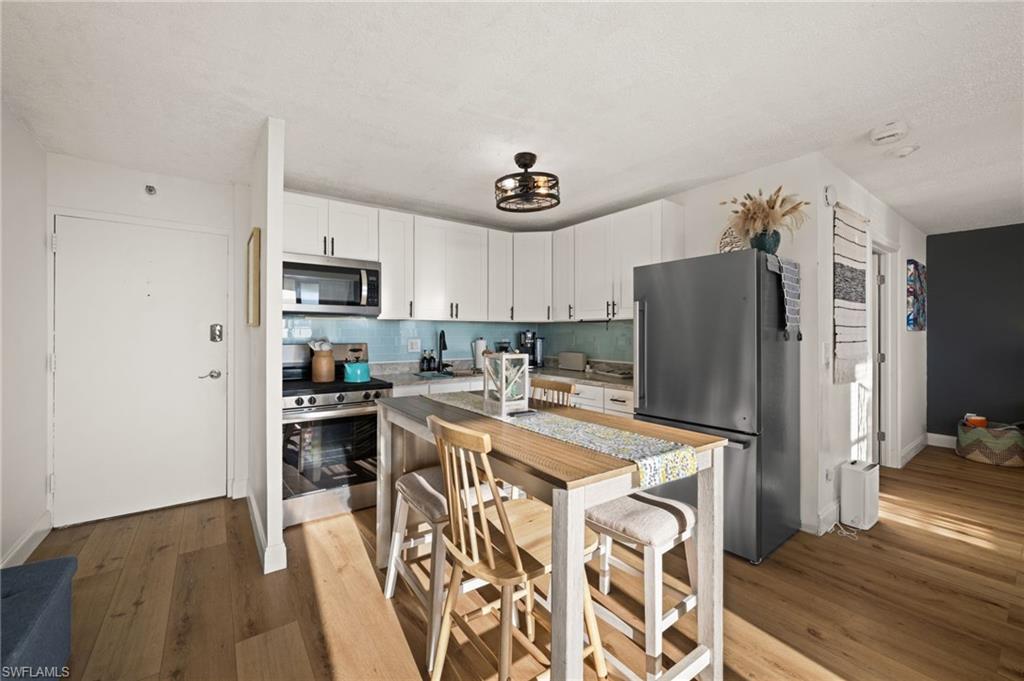 Kitchen featuring appliances with stainless steel finishes, white cabinets, decorative backsplash, light wood-style flooring, and dark countertops