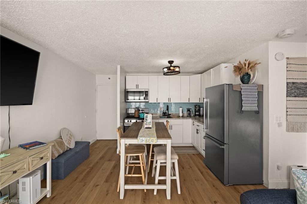 Kitchen with stainless steel appliances, tasteful backsplash, white cabinets, a textured ceiling, and light wood-style flooring