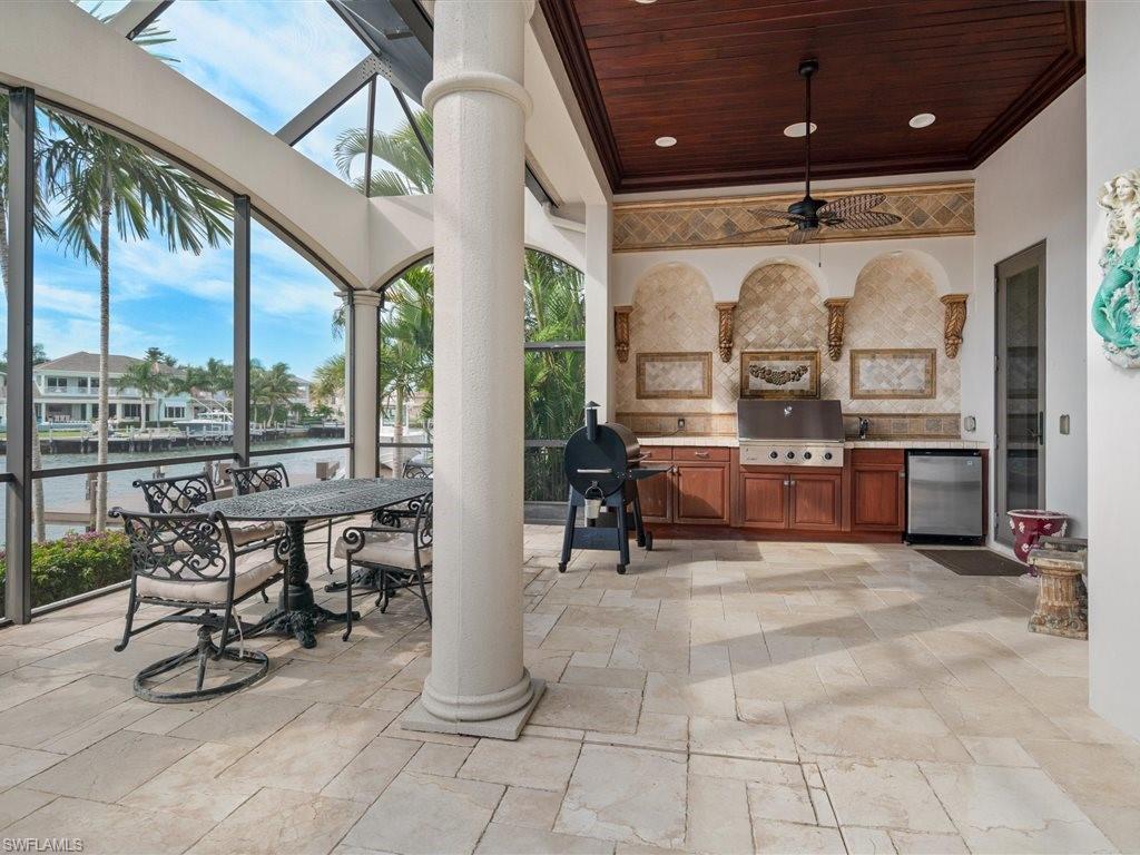 View of patio with an outdoor kitchen, ceiling fan, a sunroom, a water view, and glass enclosure