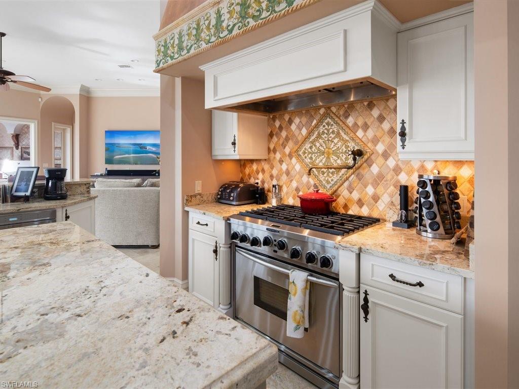 Kitchen with stainless steel gas range, light stone counters, ornamental molding, open floor plan, and custom range hood