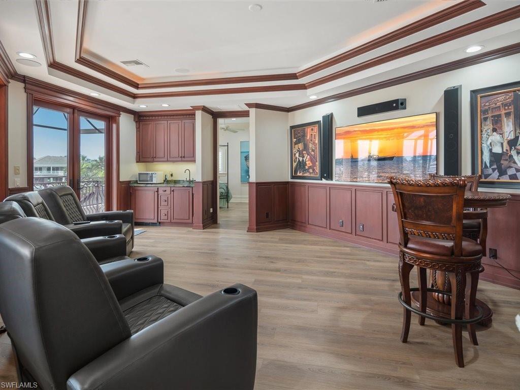 Living area featuring crown molding, a raised ceiling, a wainscoted wall, wet bar, and light wood-style flooring