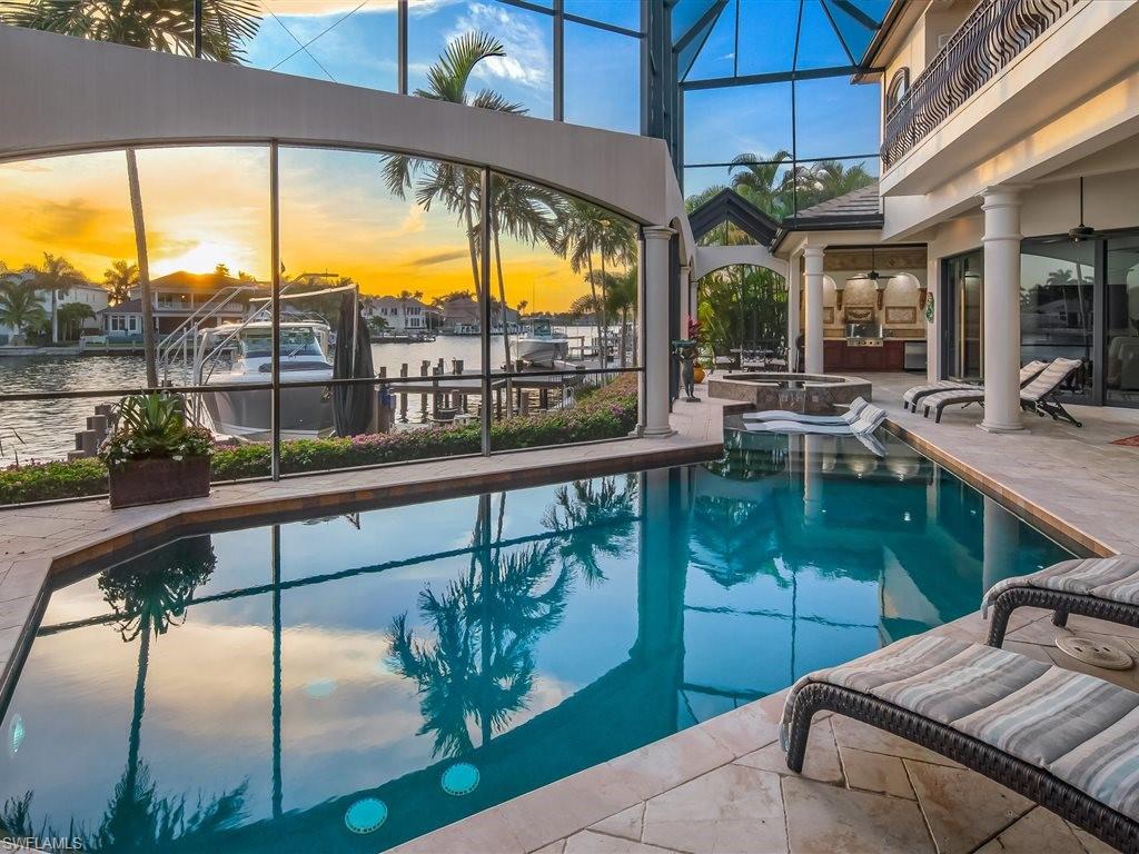 Pool at dusk featuring glass enclosure, a patio, a sunroom, a pool with connected hot tub, and a water view