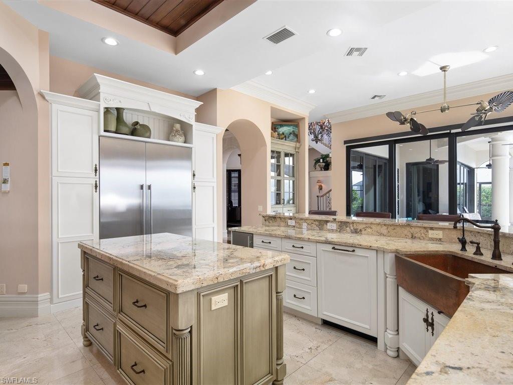 Kitchen with arched walkways, light stone counters, a kitchen island, stainless steel built in refrigerator, and white cabinetry