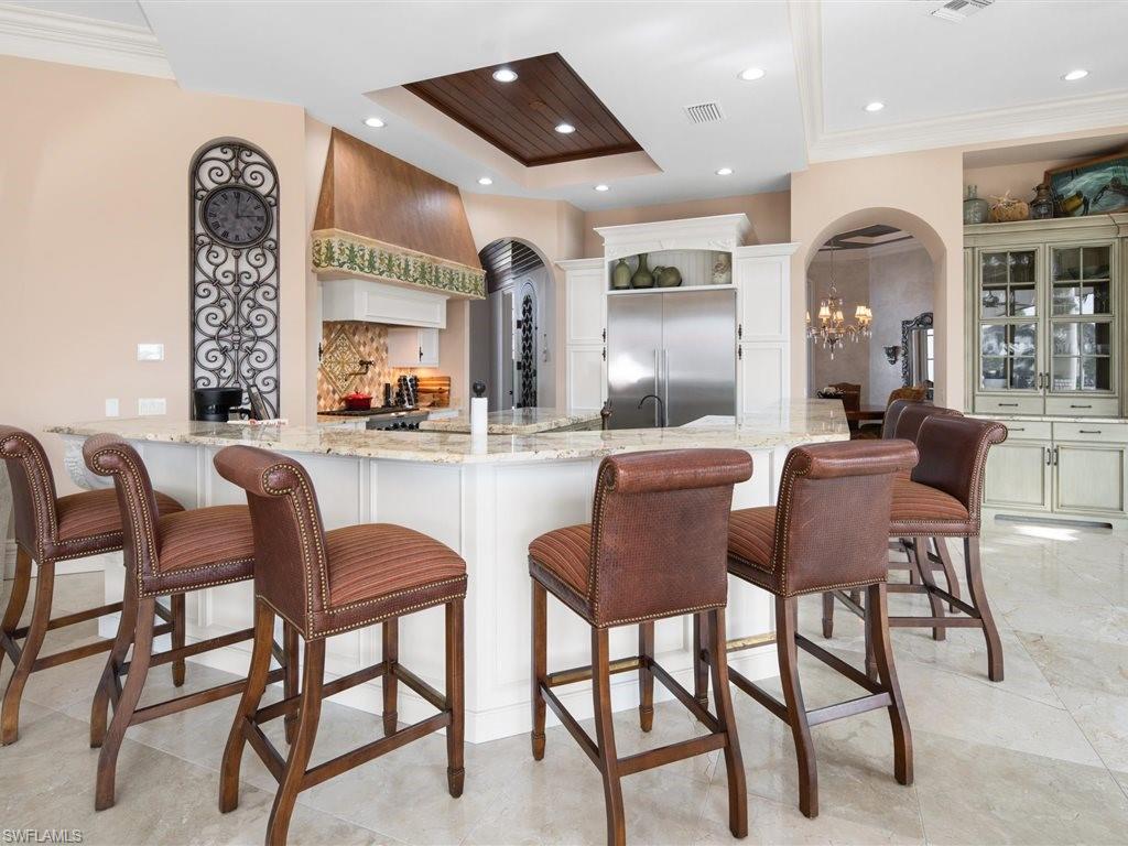 Bar featuring arched walkways, light stone countertops, stainless steel built in refrigerator, a tray ceiling, and a chandelier