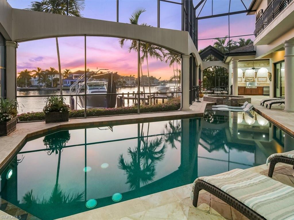 Pool at dusk featuring glass enclosure, a sunroom, a pool with connected hot tub, a water view, and a patio area