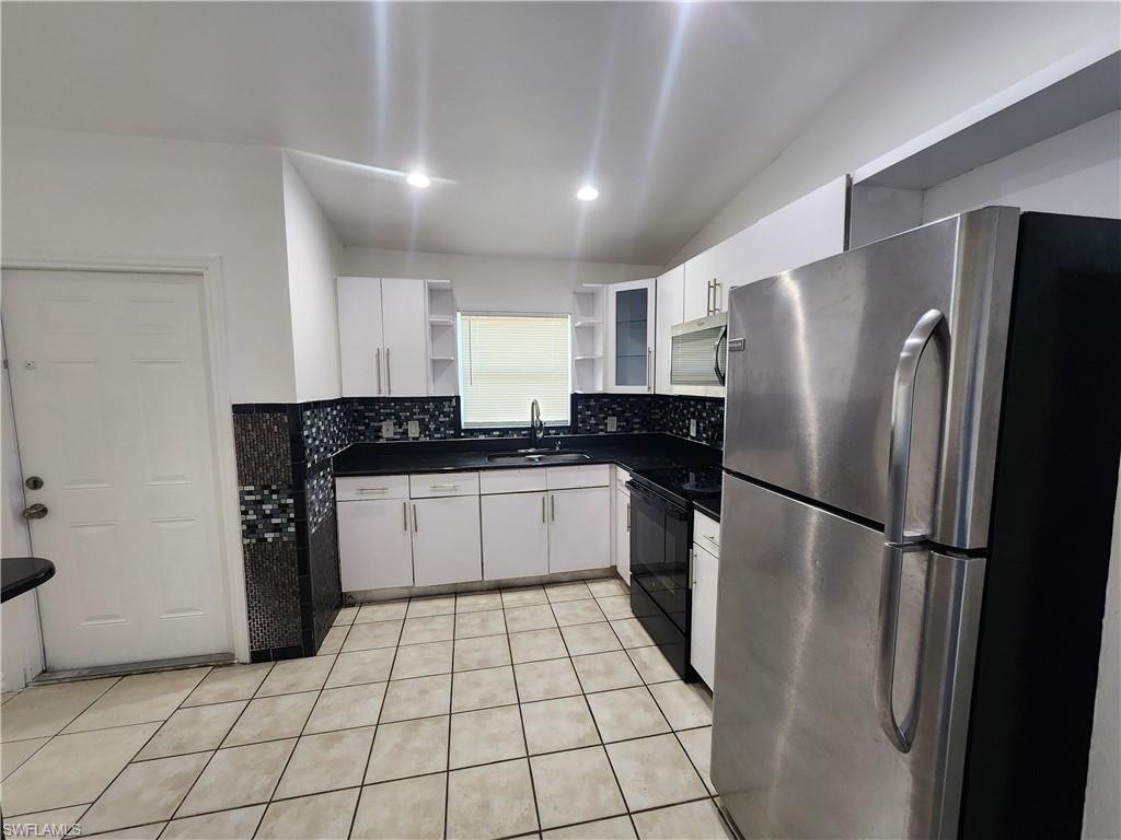 Kitchen with stainless steel appliances, dark countertops, open shelves, white cabinets, and light tile patterned flooring
