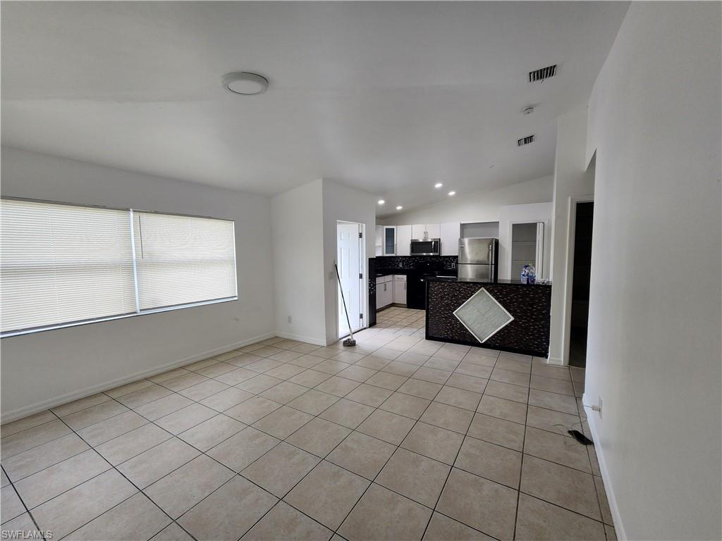 Unfurnished living room with vaulted ceiling, light tile patterned floors, and recessed lighting