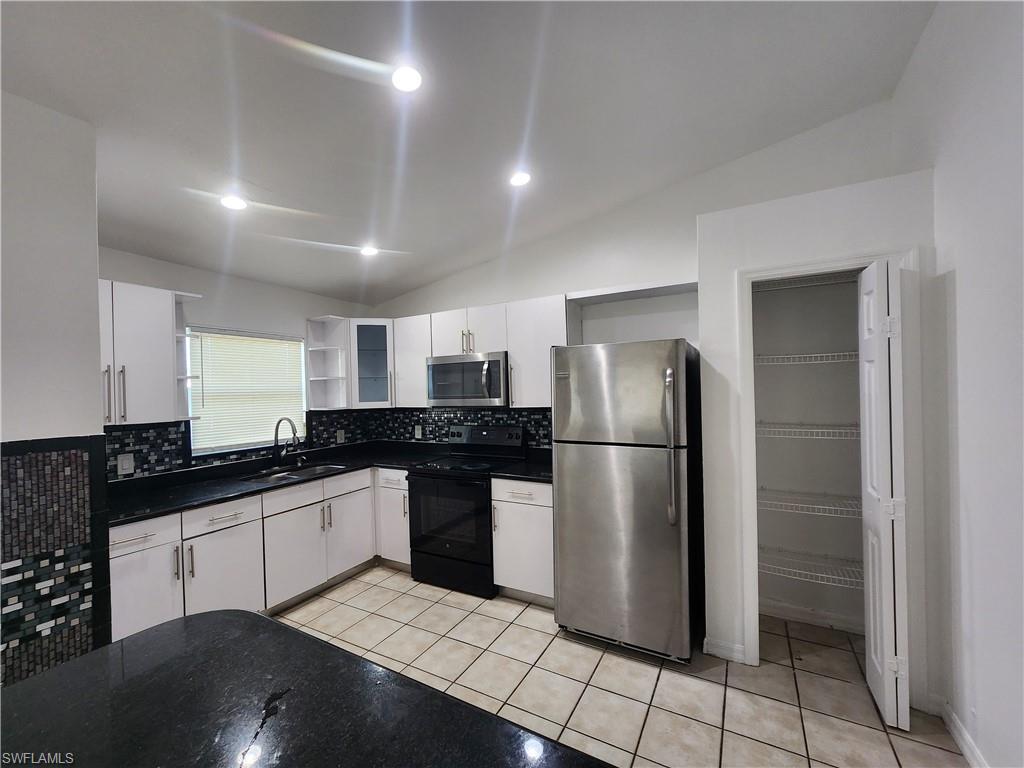 Kitchen with lofted ceiling, open shelves, stainless steel appliances, white cabinets, and light tile patterned flooring