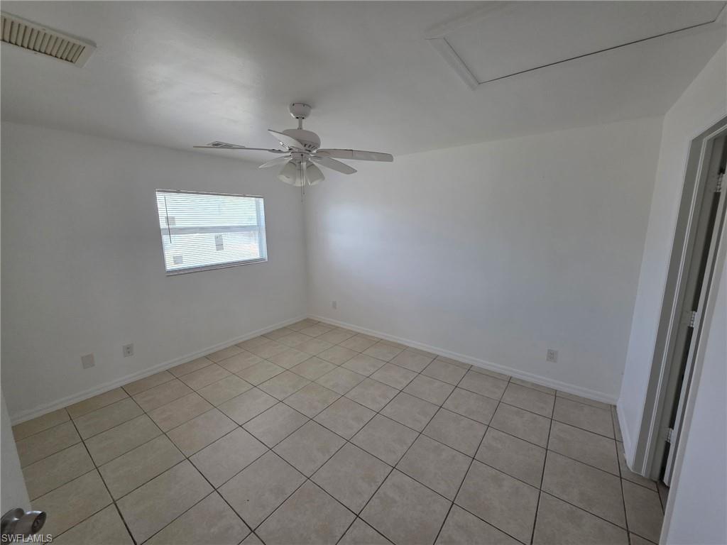 Empty room with light tile patterned floors, ceiling fan, and attic access