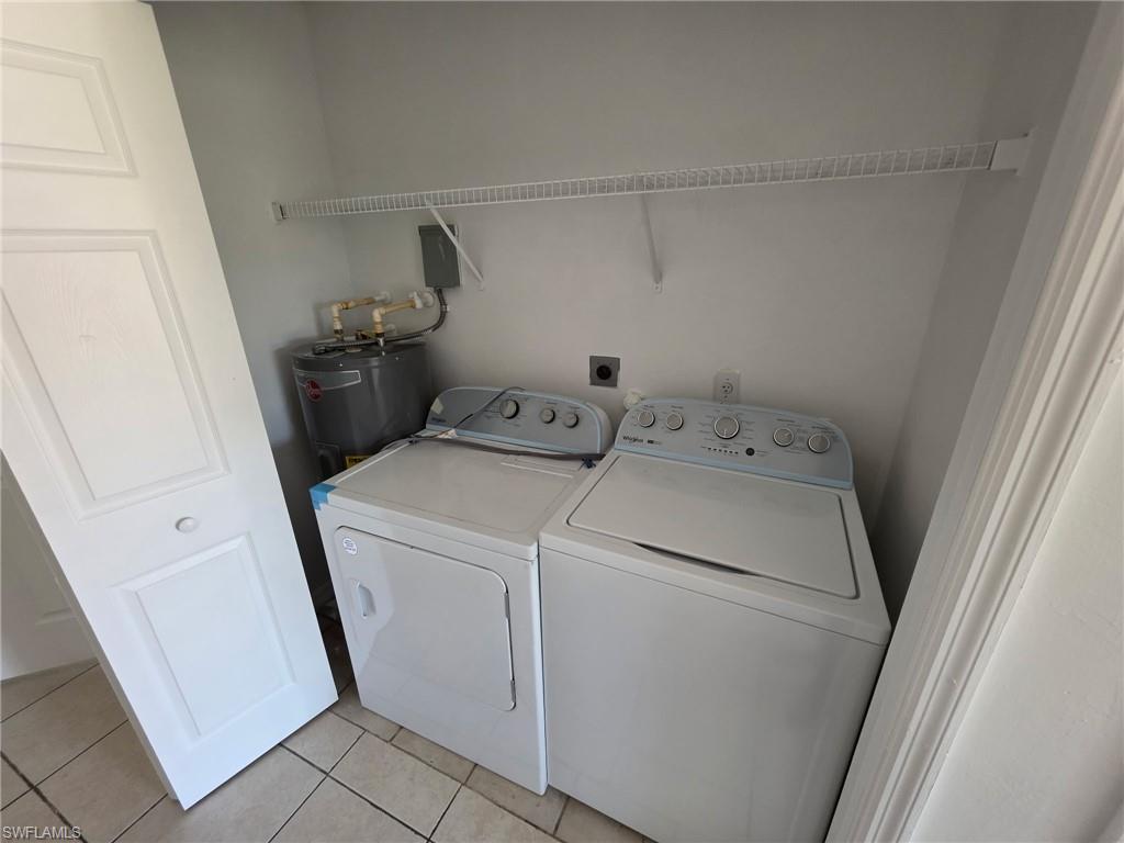Laundry room featuring washing machine and clothes dryer, electric water heater, and light tile patterned floors