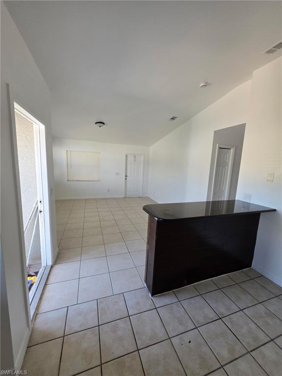 Kitchen with dark countertops, light tile patterned flooring, vaulted ceiling, and a peninsula