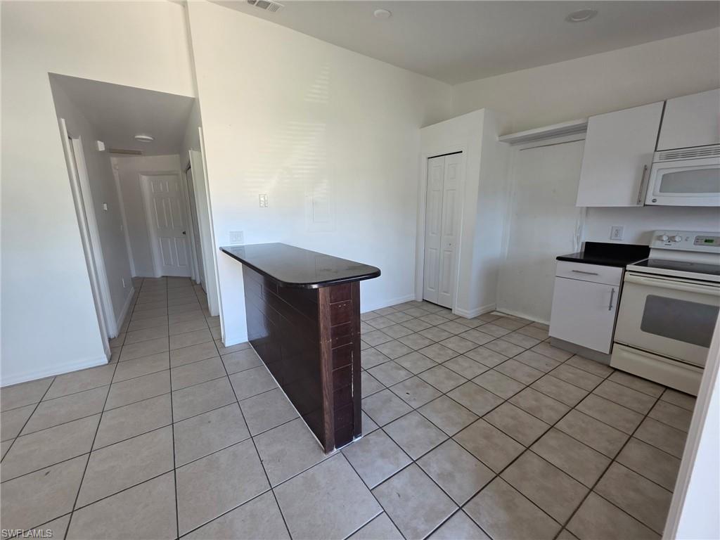 Kitchen with white appliances, dark countertops, a peninsula, white cabinets, and light tile patterned flooring