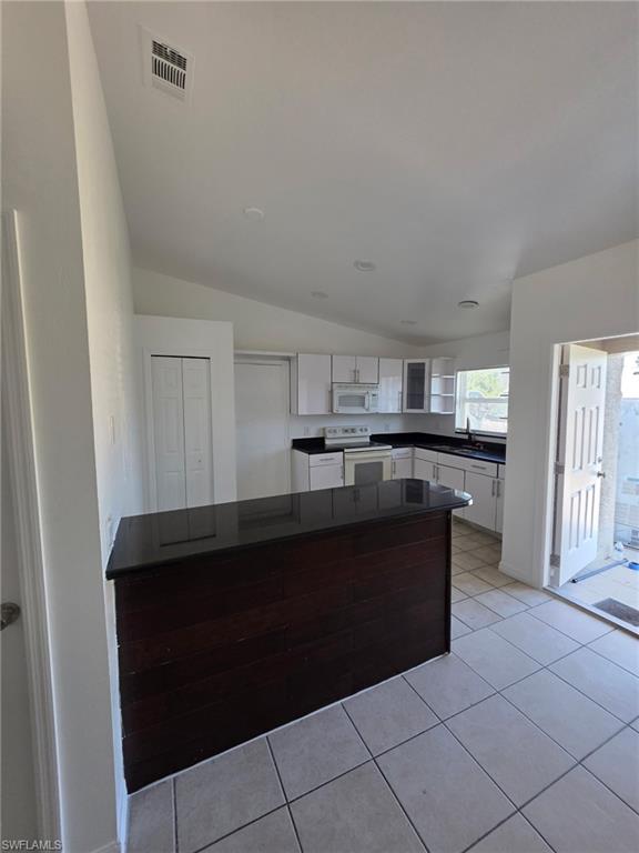 Kitchen featuring white cabinetry, white appliances, light tile patterned floors, dark countertops, and vaulted ceiling