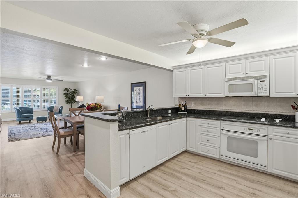 Kitchen with a ceiling fan, open floor plan, white appliances, and white cabinets