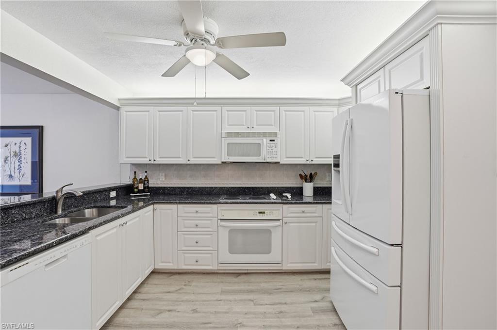 Kitchen with white appliances, dark stone counters, and white cabinetry