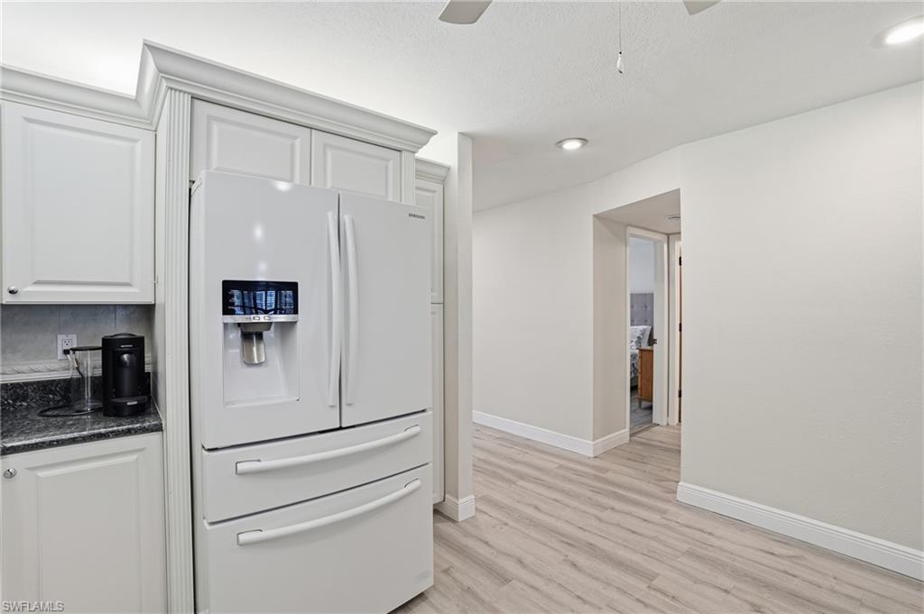 Kitchen with white refrigerator with ice dispenser, white cabinetry, dark stone counters, a ceiling fan, and light wood-type flooring