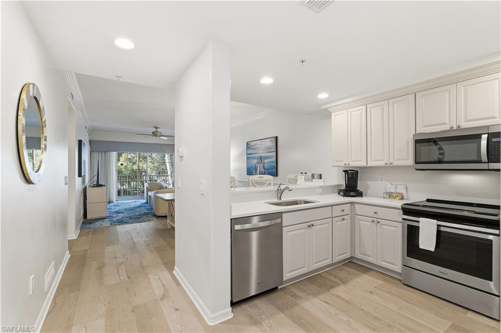 Kitchen featuring appliances with stainless steel finishes, light wood-type flooring, a ceiling fan, open floor plan, and ornamental molding