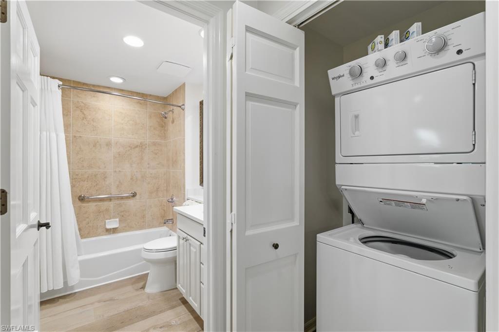 Laundry room with light wood finished floors, stacked washer / drying machine, and recessed lighting