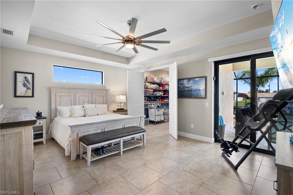 Bedroom featuring a walk in closet, access to exterior, a raised ceiling, and ceiling fan