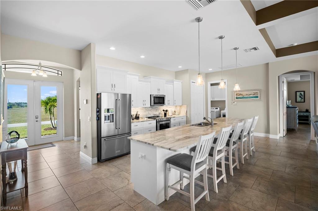 Kitchen with arched walkways, a kitchen breakfast bar, stainless steel appliances, white cabinetry, and a large island with sink