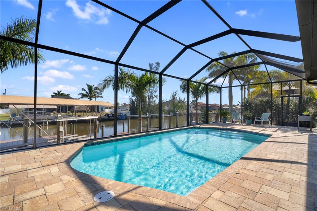 Outdoor pool with glass enclosure, a sunroom, a patio area, a water view, and a dock