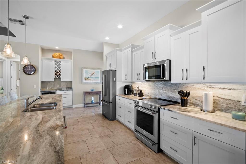 Kitchen featuring white cabinets, appliances with stainless steel finishes, decorative backsplash, hanging light fixtures, and light stone counters