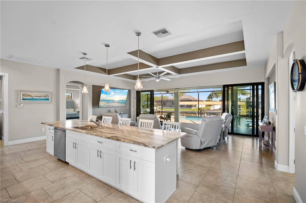 Kitchen with white cabinetry, hanging light fixtures, light stone counters, a kitchen island with sink, and coffered ceiling