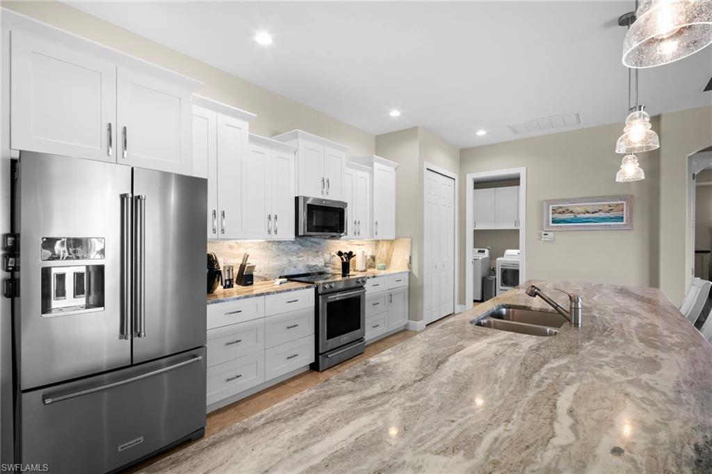 Kitchen featuring appliances with stainless steel finishes, white cabinetry, light stone counters, light tile patterned floors, and recessed lighting