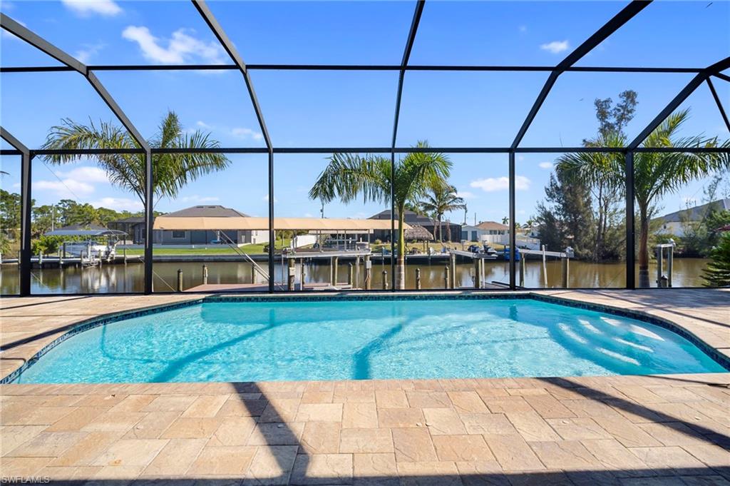 Swimming pool with boat lift, a boat dock, a sunroom, glass enclosure, and a water view