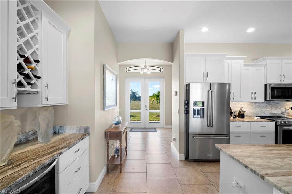 Kitchen with appliances with stainless steel finishes, backsplash, white cabinetry, light stone countertops, and wine cooler