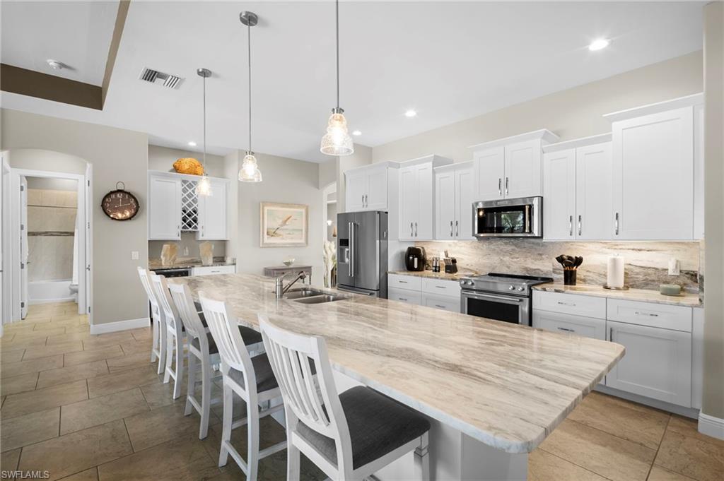 Kitchen featuring white cabinets, a kitchen breakfast bar, backsplash, appliances with stainless steel finishes, and arched walkways