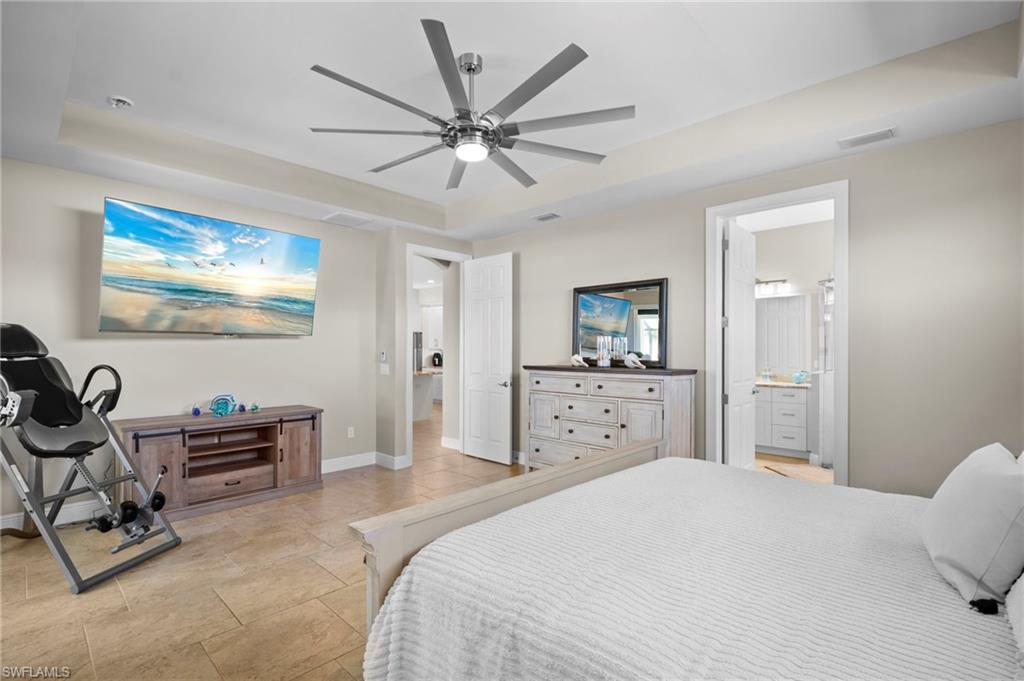 Bedroom featuring a raised ceiling, a ceiling fan, and ensuite bath