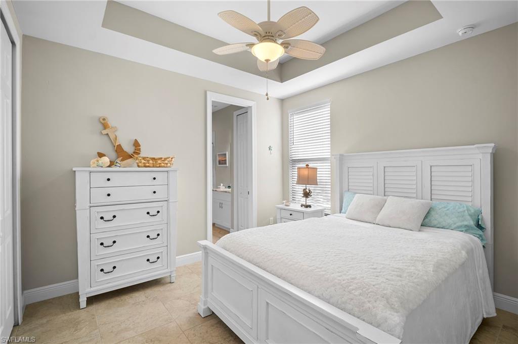 Bedroom featuring a raised ceiling, ceiling fan, connected bathroom, and light tile patterned flooring