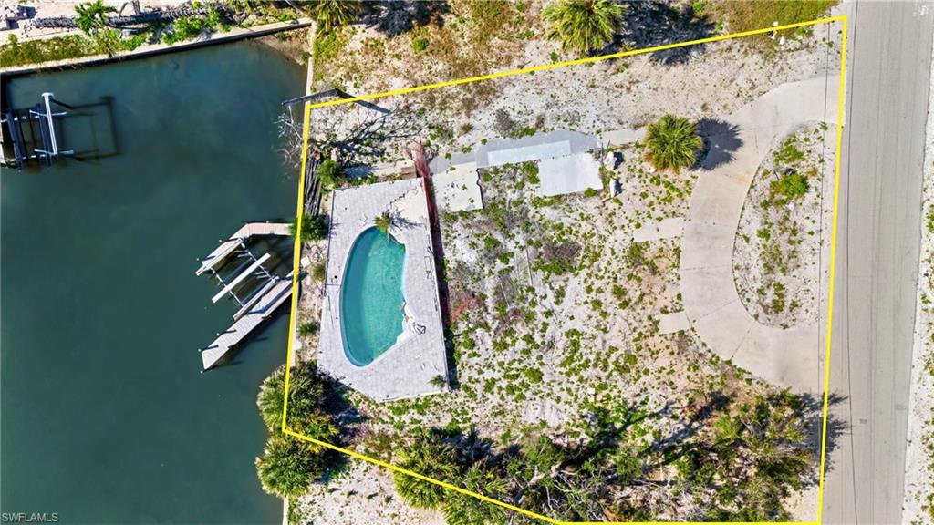 Aerial view of property and surrounding area with property boundaries highlighted, a pool, and a large body of water  - Virtually Edited Image