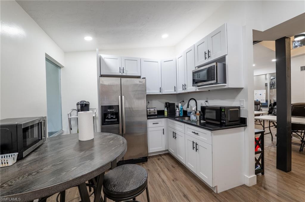 Kitchen with stainless steel appliances, light wood finished floors, white cabinetry, dark stone countertops, and recessed lighting