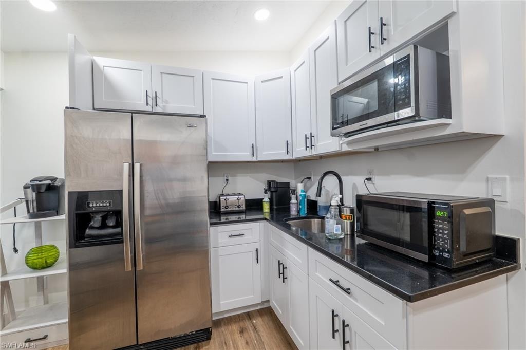 Kitchen featuring stainless steel appliances, dark stone counters, white cabinetry, light wood-style floors, and recessed lighting