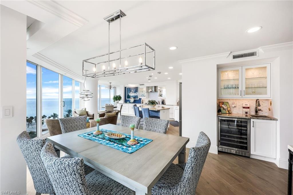 Dining space featuring ornamental molding, beverage cooler, indoor wet bar, dark wood-type flooring, and a water view
