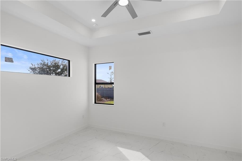 Unfurnished room featuring light marble finish floors, a raised ceiling, ceiling fan, and recessed lighting