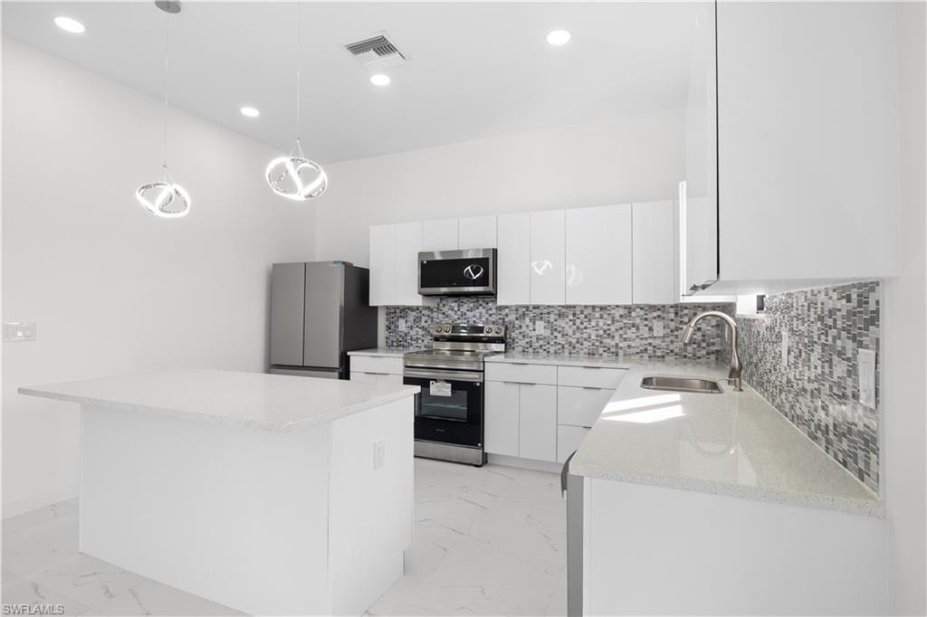 Kitchen featuring stainless steel appliances, pendant lighting, white cabinetry, a kitchen island, and light marble finish flooring