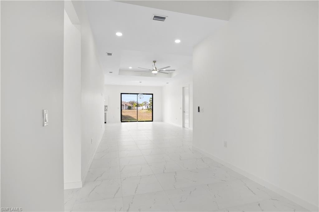 Corridor with light marble finish floors, recessed lighting, and a tray ceiling