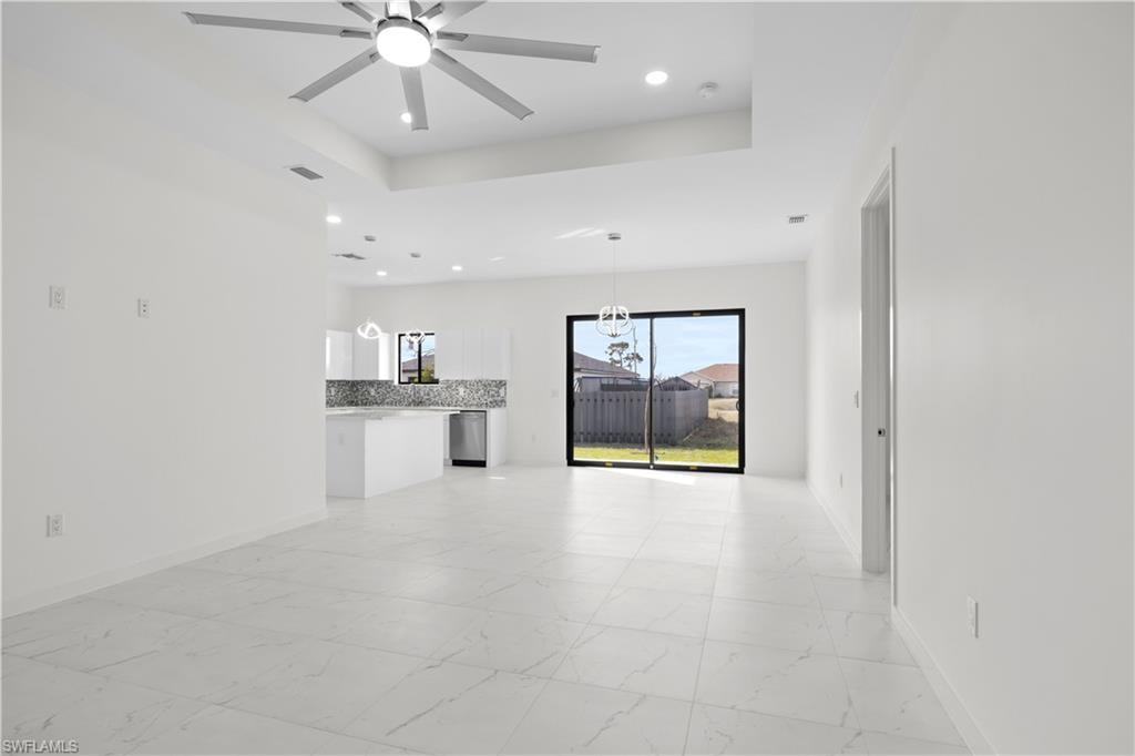 Unfurnished living room featuring a raised ceiling, light marble finish flooring, a ceiling fan, and recessed lighting